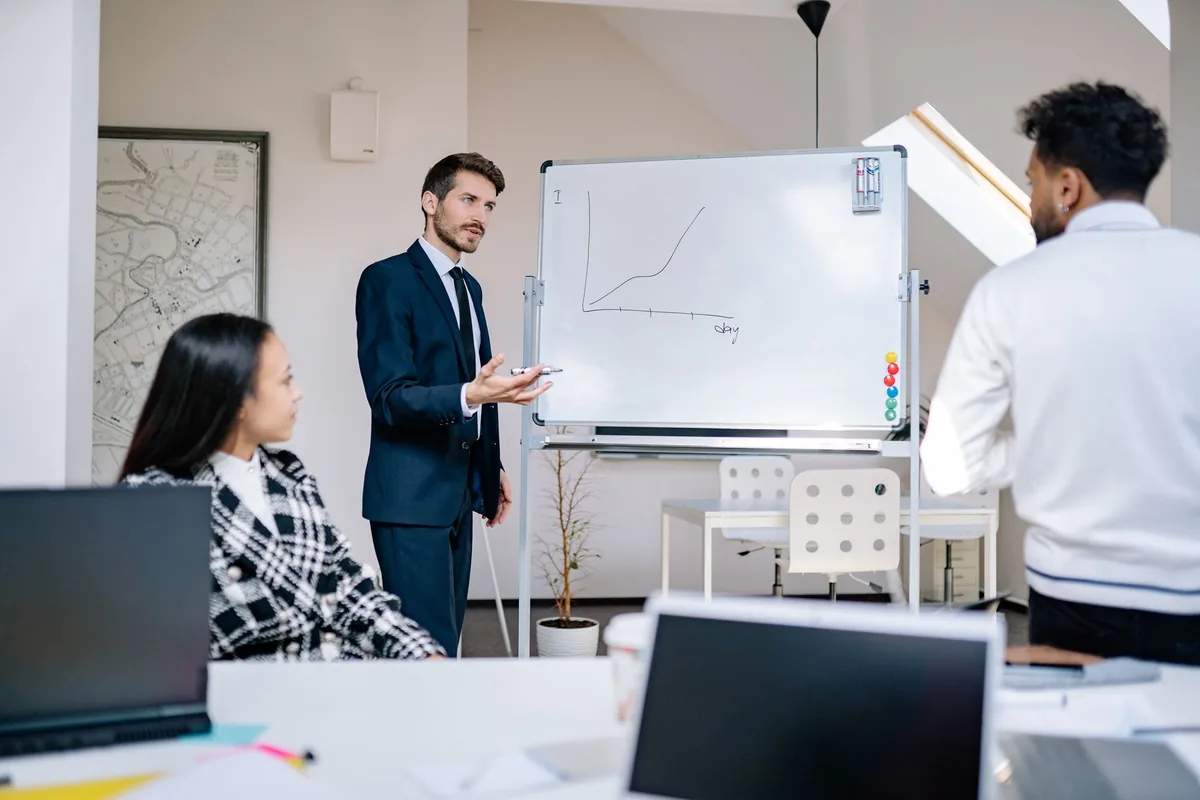 A presenter speaking to colleagues beside a whiteboard in an office
